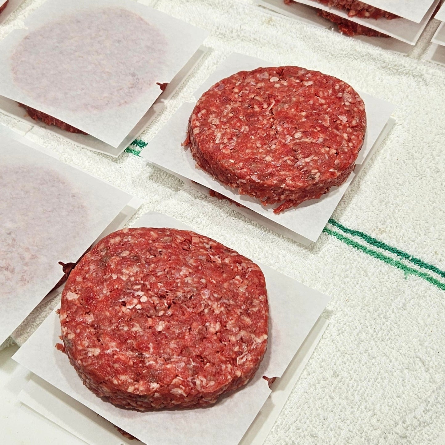 Raw ground meat patties on a cutting board with a tiled surface.